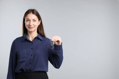 Emlakçının elinde anahtar, ev şekilli anahtarlık açık gri arka planda, metin için boşluk var.