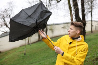 Kırık şemsiyeli bir adam açık havada yağmur altında rüzgarla savaşıyor.