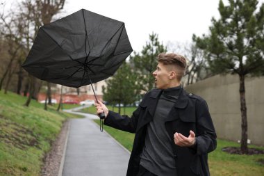 Kırık şemsiyeli bir adam açık havada yağmur altında rüzgarla savaşıyor.