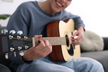 Genç adam kanepede gitar çalıyor, yakın plan.
