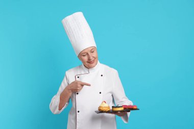 Profesyonel pasta şefi açık mavi arka plandaki tatlılara işaret ediyor.