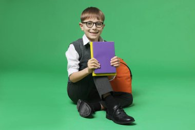 Sırt çantası ve yeşil arka plan kitapları olan tatlı bir okul çocuğu.