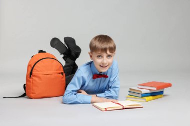 Sırt çantası açık gri arka planda kitap okuyan sevimli bir okul çocuğu.