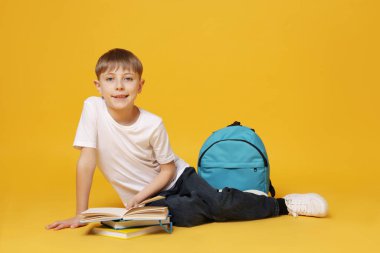 Sırt çantası turuncu arka planda kitap okuyan tatlı bir okul çocuğu.