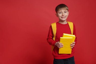 Sırt çantası ve kırmızı arkaplan kitapları olan sevimli bir okul çocuğu.