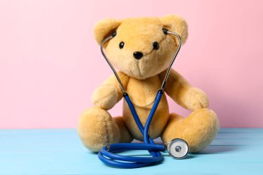 Pediatri konsepti. Açık mavi ahşap masada steteskoplu oyuncak ayı pembe arka planda