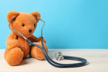 Pediatri konsepti. Açık mavi arkaplana karşı ahşap masada steteskoplu oyuncak ayı, metin için yer