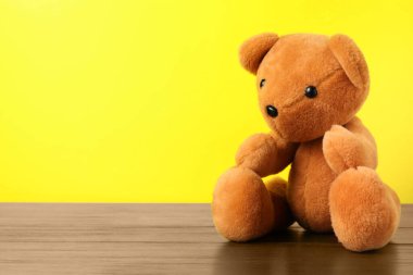 Sarı arka planda tahta masada sevimli bir oyuncak ayı. Metin için boşluk