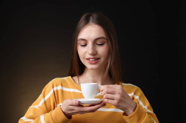 Kahverengi arka planda bir fincan kahveyle gülümseyen kadın.