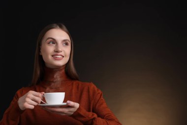 Kahverengi arka planda bir fincan kahveyle gülümseyen kadın. Metin için boşluk