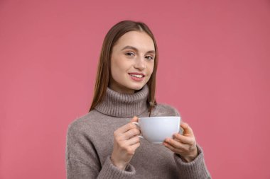 Pembe arka planda bir fincan kahveyle gülümseyen kadın.