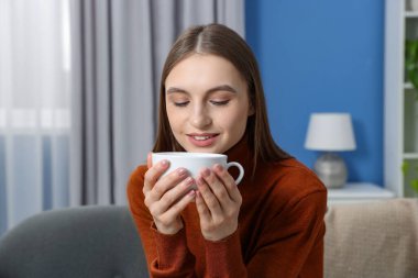 Evdeki kanepede bir fincan kahveyle gülümseyen kadın.