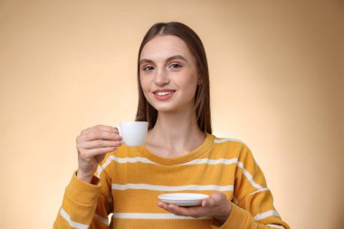 Bej renkli arka planda bir fincan kahveyle gülümseyen kadın