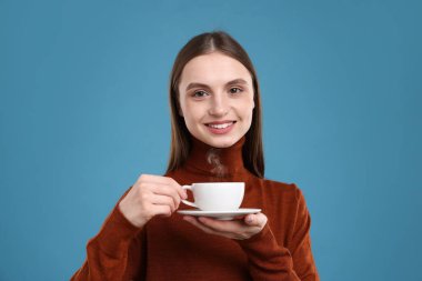 Açık mavi arka planda bir fincan kahveyle gülümseyen kadın.