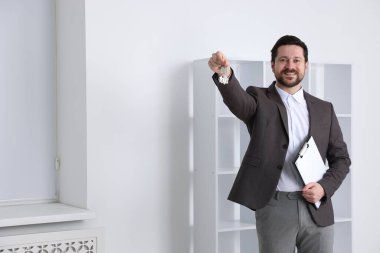 Emlakçının elinde anahtarlık, ev şeklindeki anahtarlık, kapalı alanda pano ve metin için yer var.