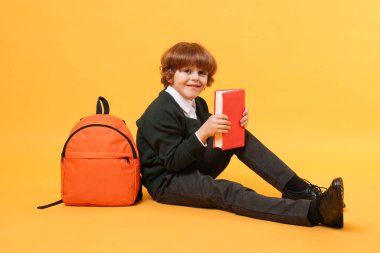Sırt çantası ve turuncu arka plan kitabı olan tatlı bir okul çocuğu.
