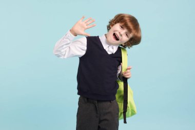 Açık mavi arka planda sırt çantası olan sevimli bir okul çocuğu.