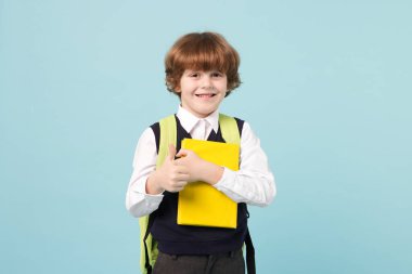 Sırt çantası ve açık mavi arka plan kitabı olan tatlı bir okul çocuğu.