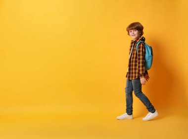 Turuncu arka planda sırt çantası olan tatlı bir okul çocuğu, mesaj için yer var.