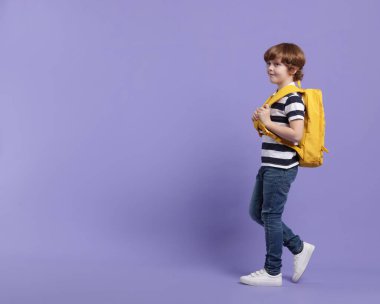 Menekşe arka planında sırt çantası olan sevimli bir okul çocuğu. Mesaj için yer var.