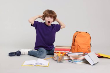 Sırt çantası, kitapları ve açık gri arka planda farklı kırtasiyeleri olan sevimli bir okul çocuğu.