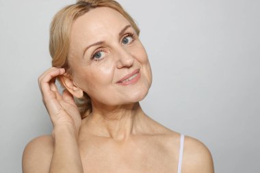 Gri arka planda gülümseyen orta yaşlı kadın portresi