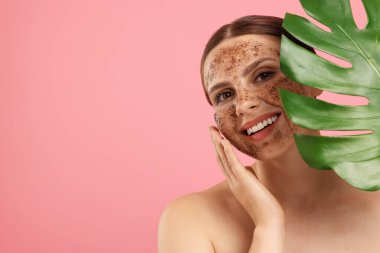 Yüzünde vücut fırçası ve pembe arka planda canavar yaprağı olan gülümseyen bir kadın. Metin için boşluk