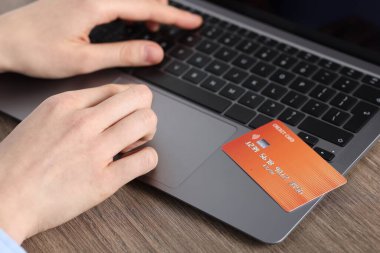 Çevrimiçi ödeme. Kredi kartlı bir kadın, ahşap masada dizüstü bilgisayarda yazı yazıyor.