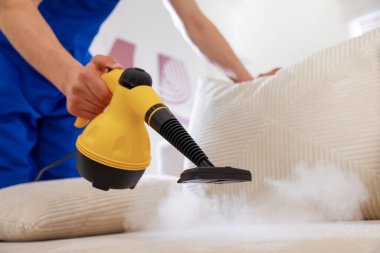 Temizlikçi kanepeyi evde buharlı temizleme makinesiyle temizliyor.