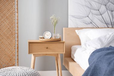 Komodinin yanında çalar saat, vazoda çiçekler ve yatağın yanında bir bardak su.