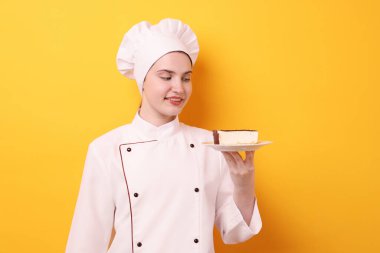 Üniformalı bir şekerci turuncu arka planda lezzetli bir pasta tutuyor.