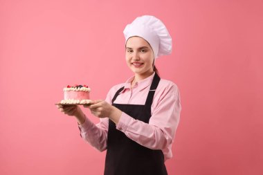 Şekerci pembe arka planda lezzetli bir pasta tutuyor.