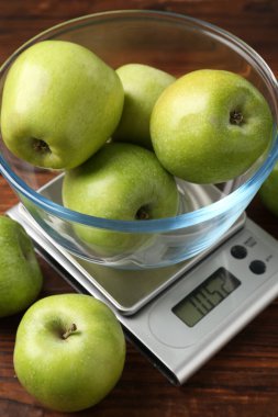 Elektronik mutfak terazisi, ahşap masada yeşil elma kasesi, yakın plan.