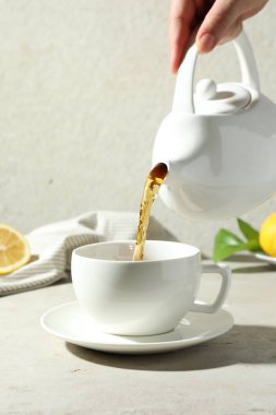 Hafif desenli masada çaydanlıktan fincana aromatik çay döken kadın, yakın plan.