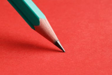 Kırmızı arka planda keskin bir grafit kalem, yakın plan. Metin için boşluk