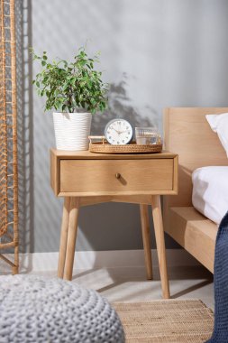 Yatağın yanında ev bitkisi, çalar saat ve yatağın yanında bir bardak su olan komodin.