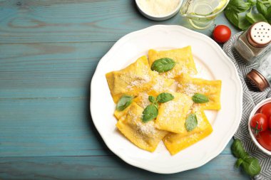 Açık mavi ahşap masada servis edilen peynirli ve fesleğenli lezzetli ravioli. Metin için boşluk