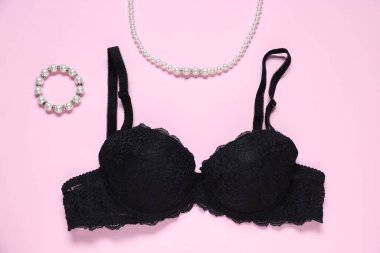 Pembe arka planda siyah dantelli sütyen ve mücevher.