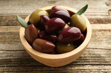 Lezzetli marine edilmiş zeytinler kasede ve ahşap masada yeşil yapraklar, yakın plan.