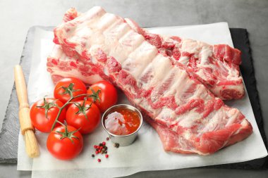 Çiğ domuz kaburgası, domates ve baharatlar gri masada, yakın plan.