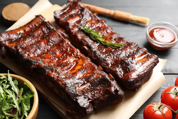 Biberiye, domates, sos ve salata ile servis edilen kızarmış domuz kaburgaları siyah ahşap masada, yakın plan.