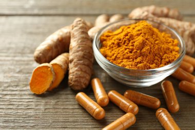 Zerdeçal kapsülleri, toz ve kökler ahşap masanın üzerinde, yakın plan.