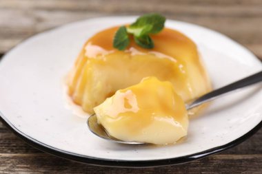 Karamel soslu lezzetli puding ve ahşap masada servis edilen nane, yakın plan.