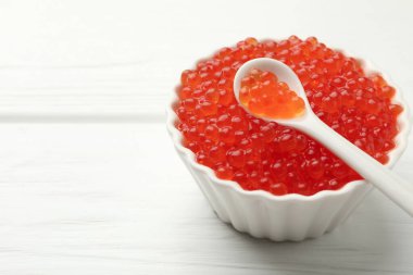 Lezzetli kırmızı havyar kasede ve kaşıkla beyaz ahşap masada, yakın plan. Metin için boşluk