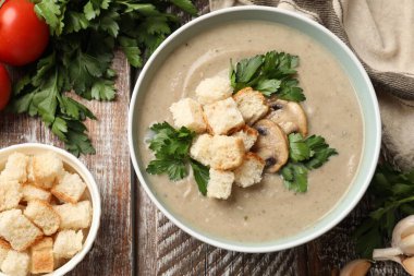 Lezzetli mantar kremalı çorba, kızarmış ekmek ve ahşap masadaki malzemeler.