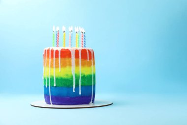 Açık mavi arkaplanda yanan mumlarla nefis gökkuşağı doğum günü pastası, metin için yer