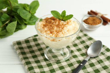 Tarçınlı lezzetli sütlaç, beyaz ahşap masada nane ve kaşık, yakın plan.