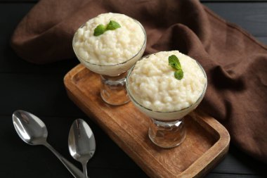 Nane şekerli lezzetli sütlaç ve siyah ahşap masada kaşıklar, yakın plan.