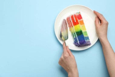 Açık mavi masada nefis bir parça gökkuşağı pastası ve spatulası olan bir kadın. Metin için boşluk