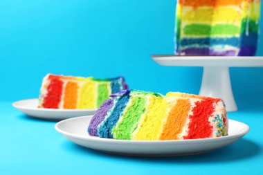 Lezzetli gökkuşağı pastası parçaları açık mavi masada, yakın plan.